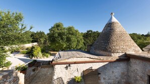 Um edifício de pedra com telhado cónico, paredes de pedra e um pequeno jardim com plantas em vasos.