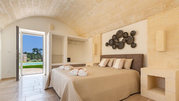 Un dormitorio con una cama grande, una chimenea de piedra y vistas a un jardín a través de una puerta abierta.