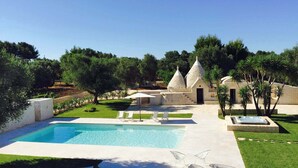 Una piscina con sillas de descanso, un edificio de piedra con techos cónicos y un césped cuidado.