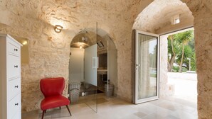 Una habitación con paredes de piedra, una silla roja, una puerta de cristal que da al exterior y un armario blanco.