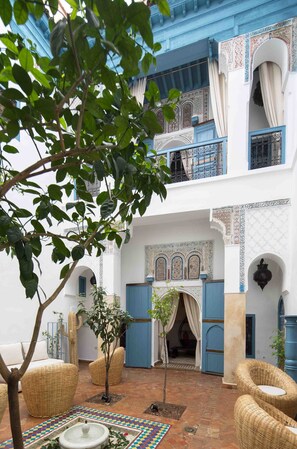 A courtyard with a fountain, wicker furniture, and a tree. - Riad Assala (Marrakech)