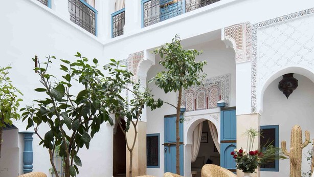 Un patio con arquitectura tradicional en azul y blanco, muebles de mimbre y una planta de cactus.