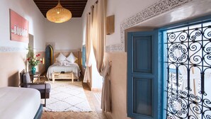 Habitación de hotel con cama, escritorio, silla, ventana con rejas decorativas y lámpara colgante.