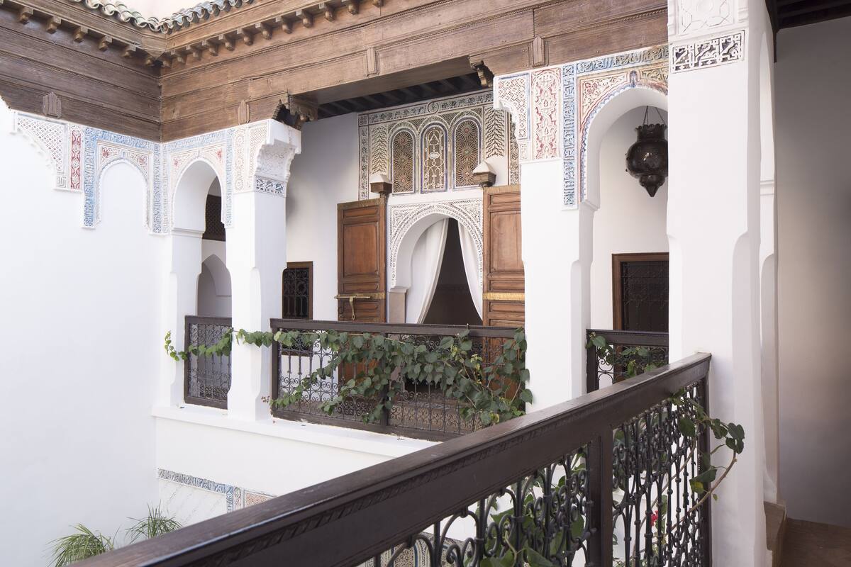 A courtyard with arches, a wooden ceiling, and a balcony with a wrought iron railing.