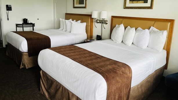 A hotel room with two beds, a desk with a telephone, and two framed artworks on the walls. - The Pines Country Inn (Owosso)