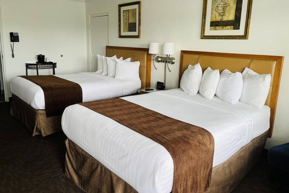 Una habitación de hotel con dos camas, un escritorio con teléfono y dos cuadros enmarcados en las paredes.