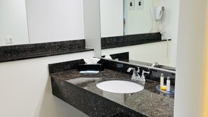 A modern bathroom with a granite countertop, a white sink, and a large mirror. - The Pines Country Inn (Owosso)