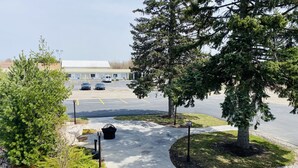 A parking lot with two cars, a building in the background, and a pathway leading to a building entrance. - The Pines Country Inn (Owosso)