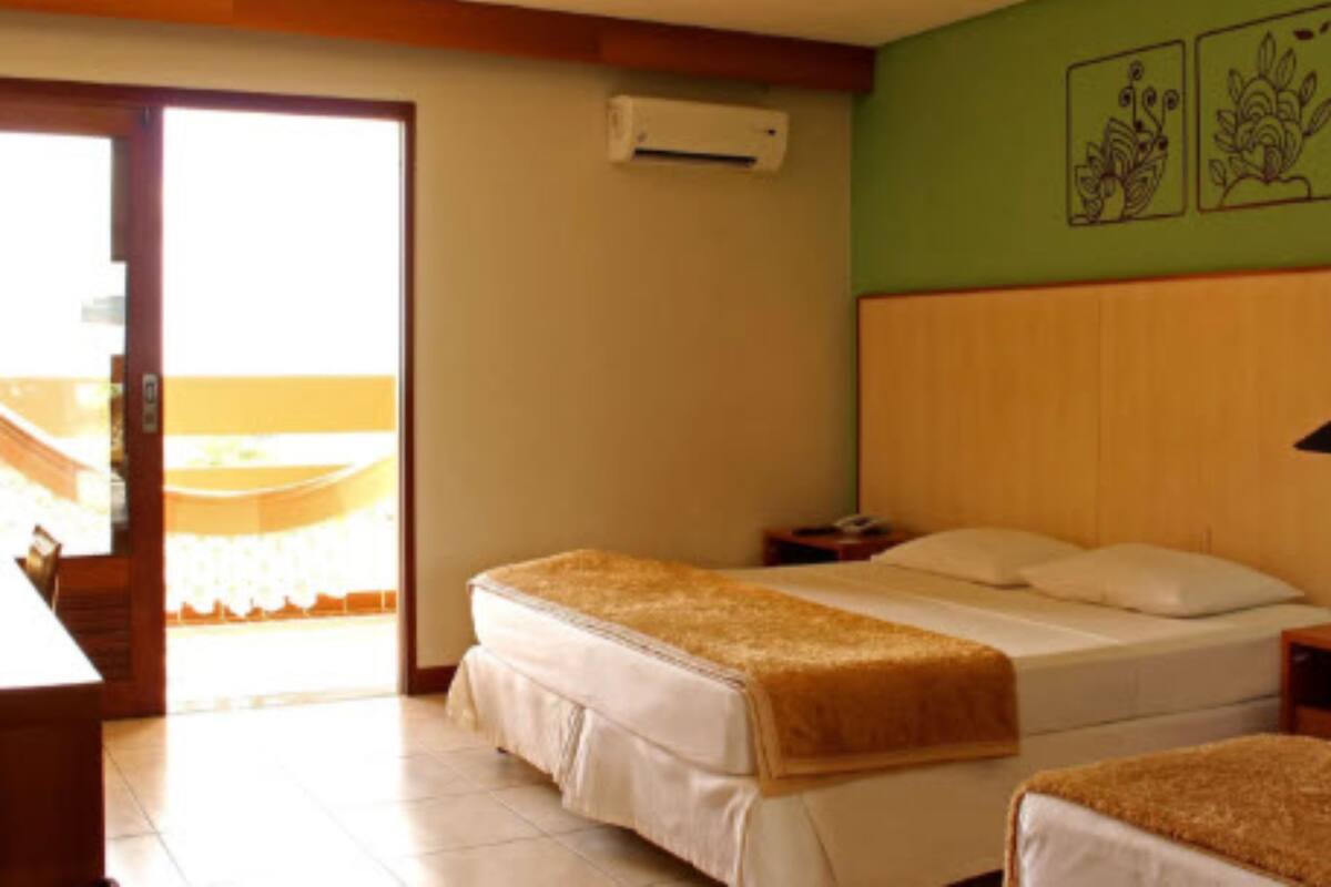 A hotel room with two beds, a wooden headboard, a small bedside table, an air conditioning unit, and a view through a glass door.