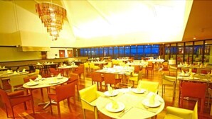 A spacious dining area with multiple tables and chairs, large windows, and a chandelier. - Garden Hotel Campina Grande (Campina Grande)