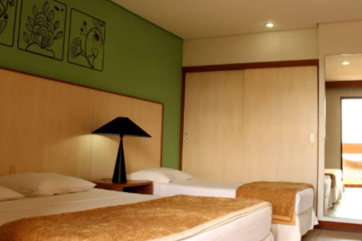A hotel room with two beds, a wooden headboard, a nightstand with a lamp, and artwork on the wall.