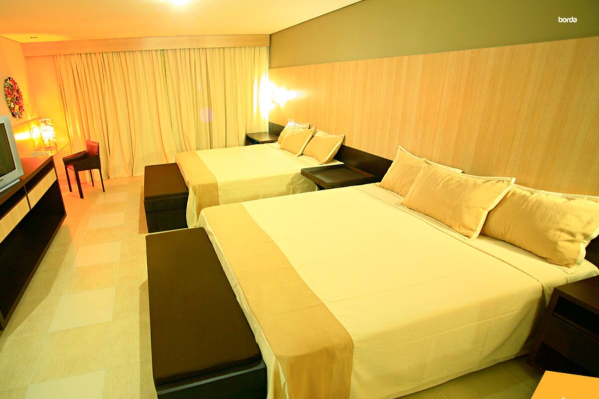A hotel room with two beds, a desk, and a television.