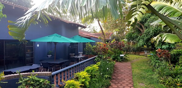 An outdoor patio with tables and chairs, surrounded by lush greenery and a pathway. - Santa Lucia Guest House (St. Lucia)