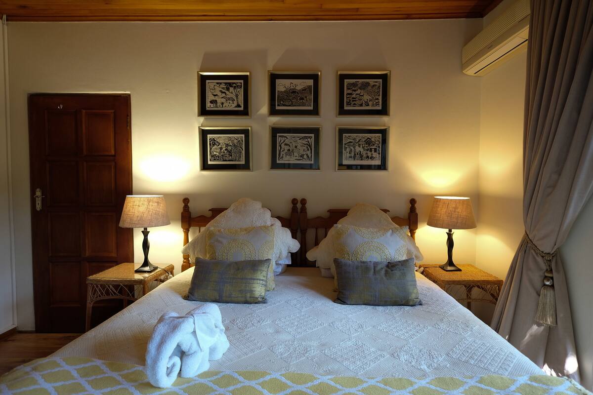 A hotel room with a large bed, two bedside tables with lamps, a wooden door, and six framed pictures on the wall.