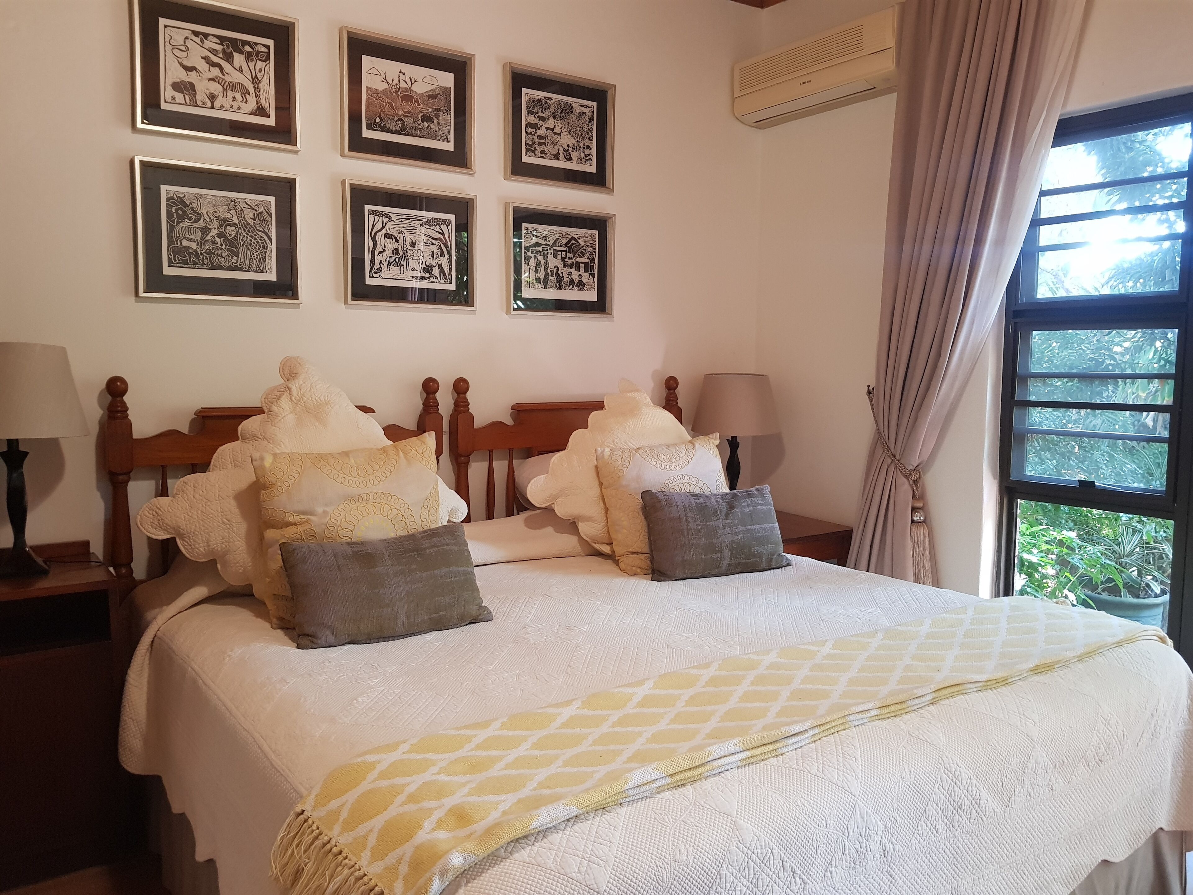 A neatly made bed with a white and yellow patterned bedspread, flanked by two nightstands with lamps, and a wall adorned with framed black and white artwork.