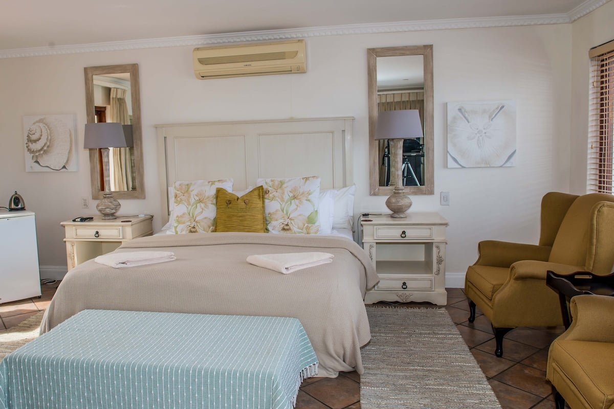 A neatly arranged bedroom with a bed, bedside tables, a lamp, a chair, and a small refrigerator.