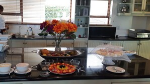 Een ontbijtbuffet met diverse gerechten en een persoon die in de achtergrond eten bereidt.