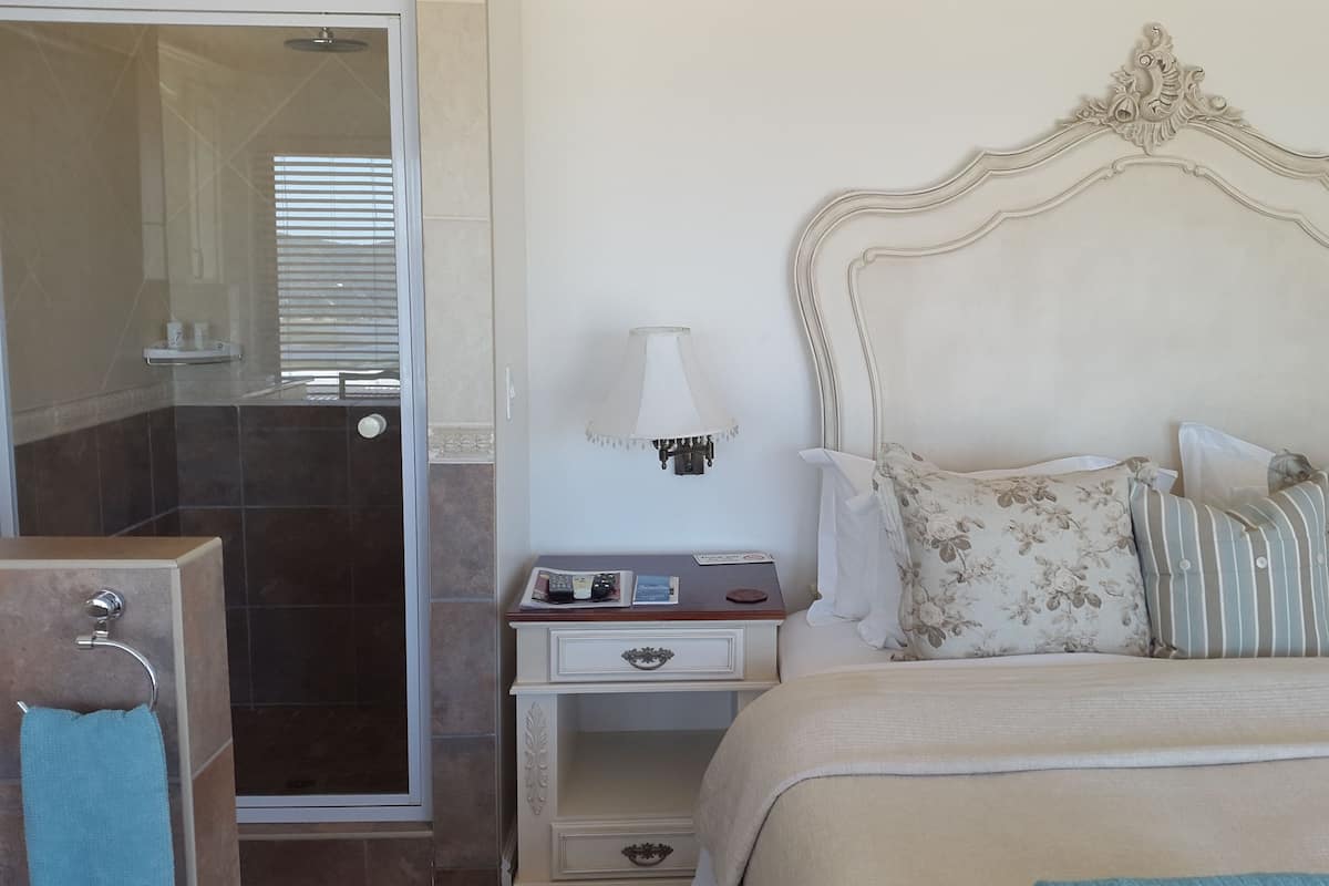 A hotel room with a bed, a nightstand, a lamp, a shower area, and a towel rack.