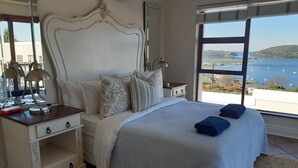 Een slaapkamer met een groot bed, een nachtkastje, een dressoir en uitzicht op zee.
