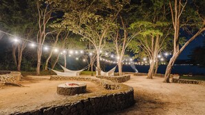 Un espace extérieur doté de murs en pierre, de hamacs et de guirlandes lumineuses.