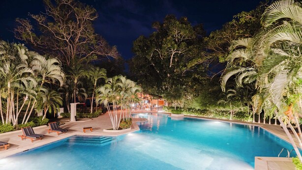 Un espace piscine aménagé pour la nuit, avec des chaises longues et des palmiers.