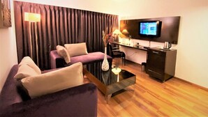 A modern living room with a sofa, a coffee table, a desk, and a flat-screen TV mounted on the wall. - RnB Banjara Hills (Hyderabad)