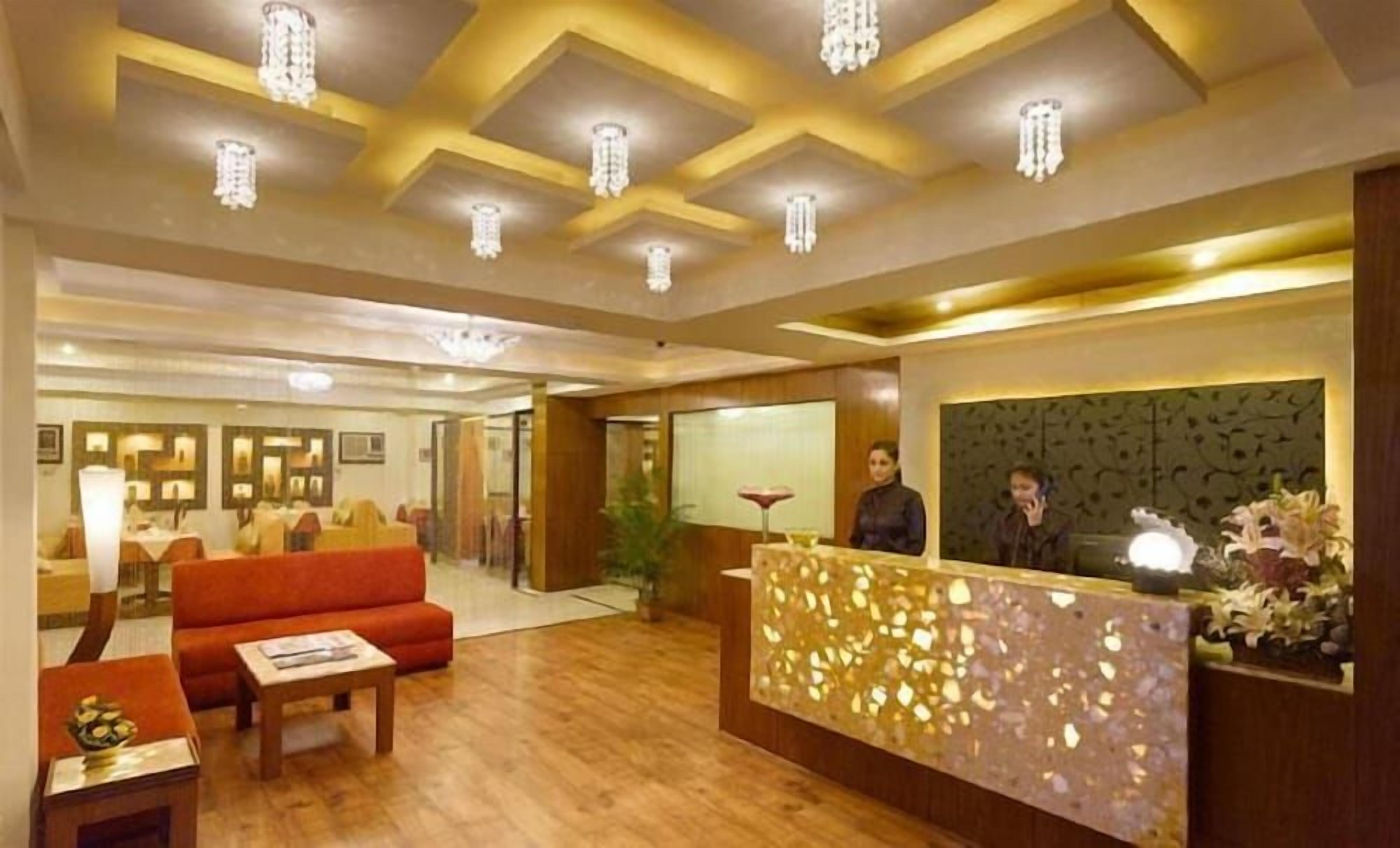 A hotel reception area with a wooden reception desk, a red sofa, and a chandelier.