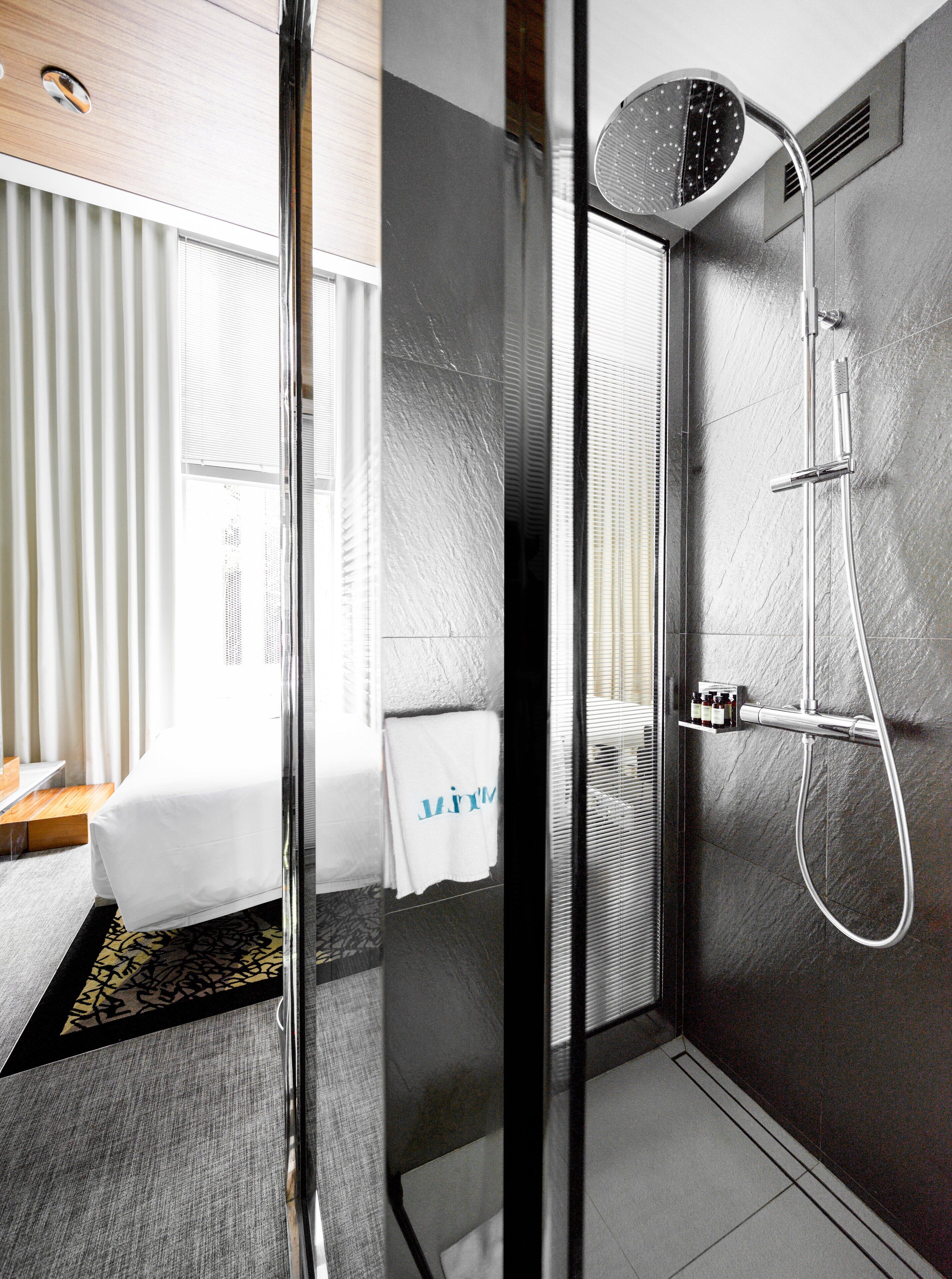 Un baño de hotel moderno con cabina de ducha de vidrio, una bañera blanca y un perchero con una toalla colgada.