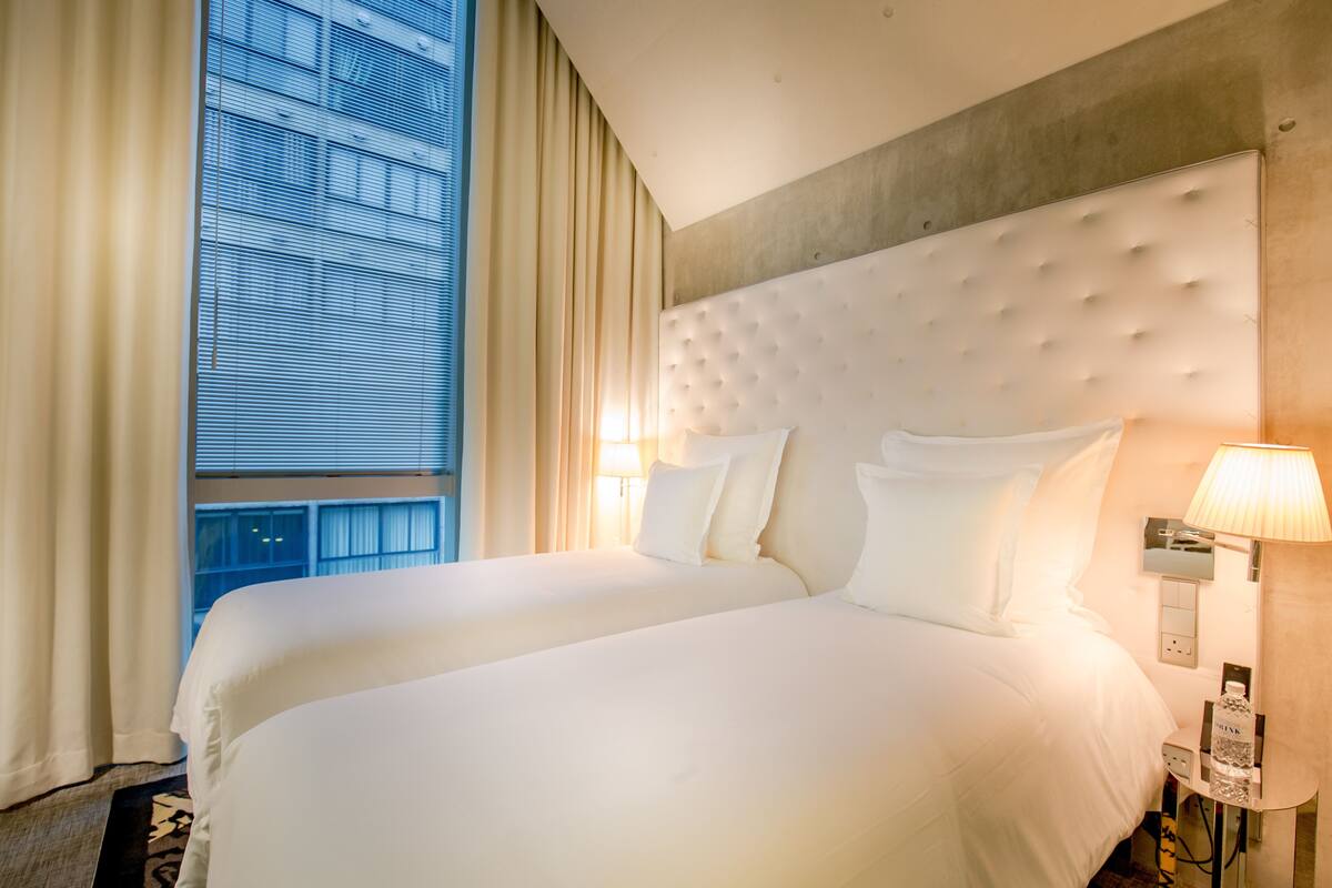 Een hotelkamer met een groot bed, een hoofdbord, een nachtkastje met een lamp en een raam met gordijnen.