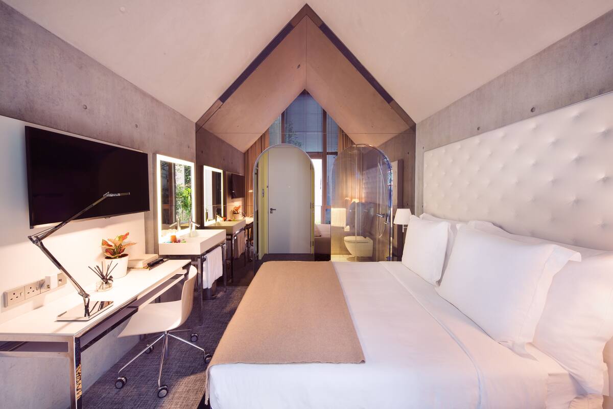 Een moderne hotelkamer met een groot bed, een bureau met een computer, een televisie en een badkamer met douche.