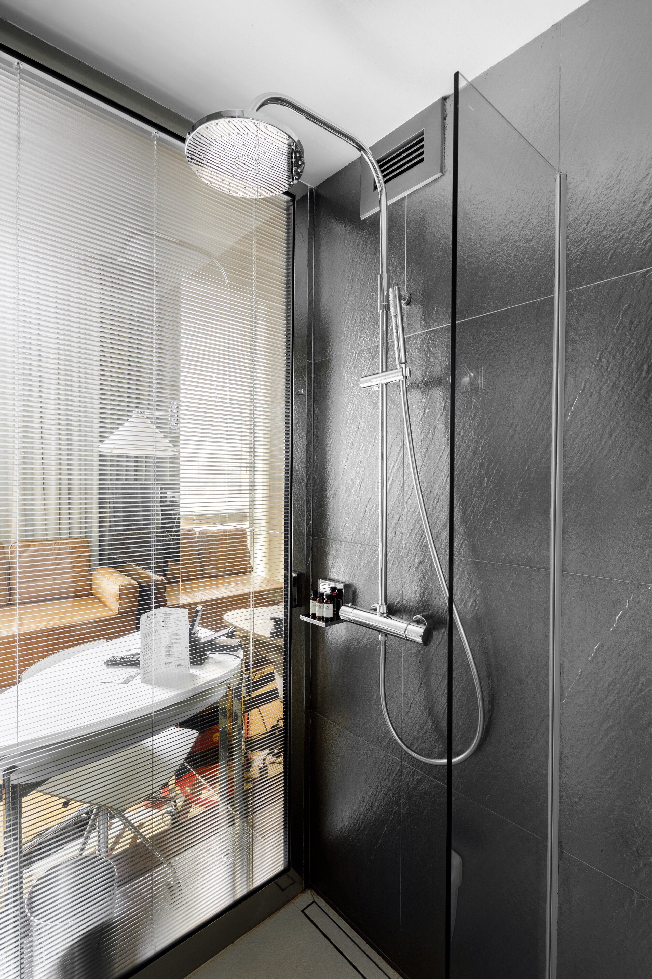 Un baño moderno con cabina de ducha de vidrio, un lavabo blanco y una pared revestida de baldosas oscuras.