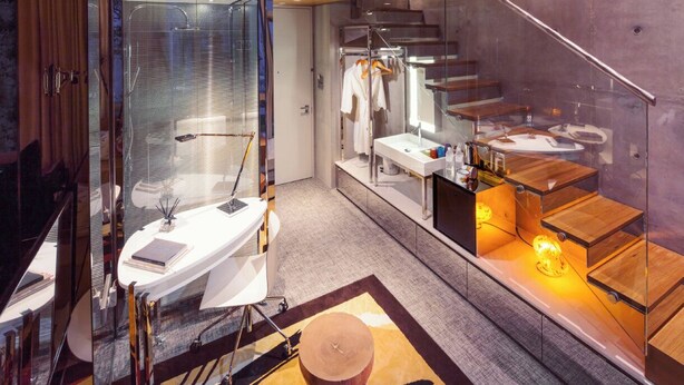 Un baño moderno con ducha envuelta en cristal, un tocador con espejo y una escalera de madera.
