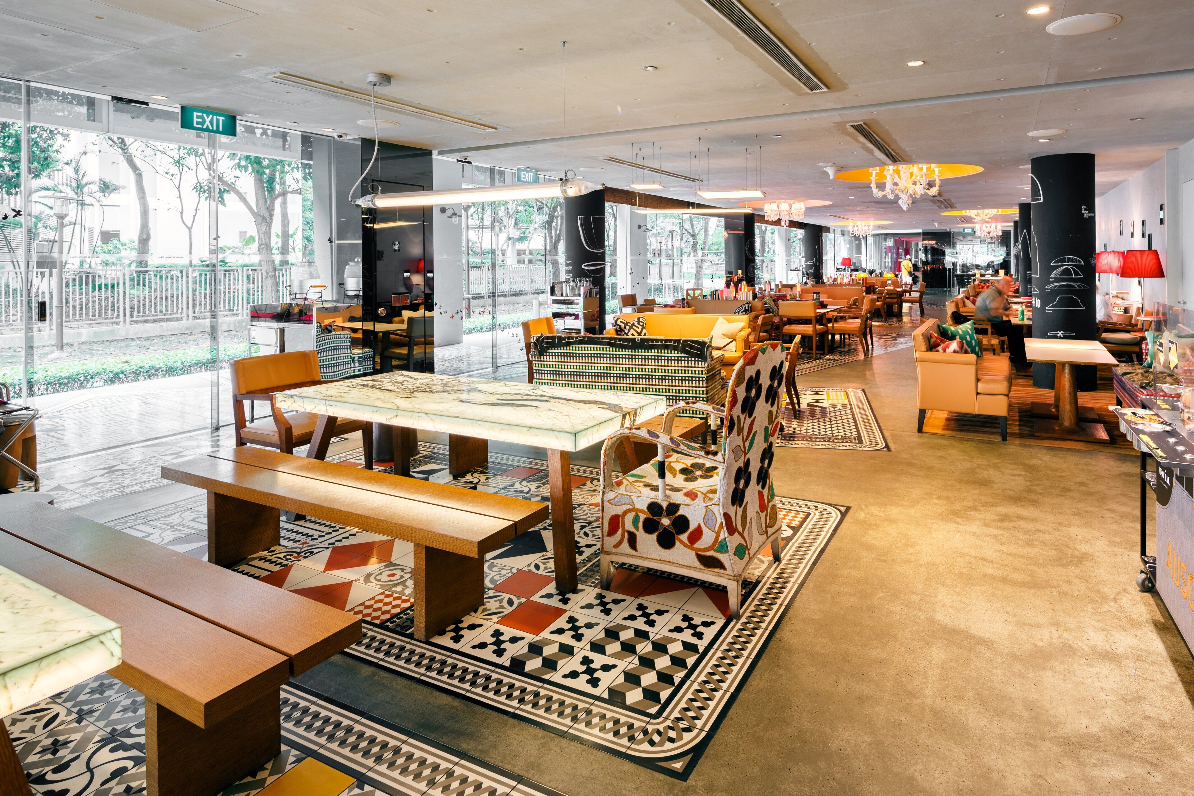 Un restaurante moderno con mesas y bancos de madera, alfombras estampadas y vistas al exterior.