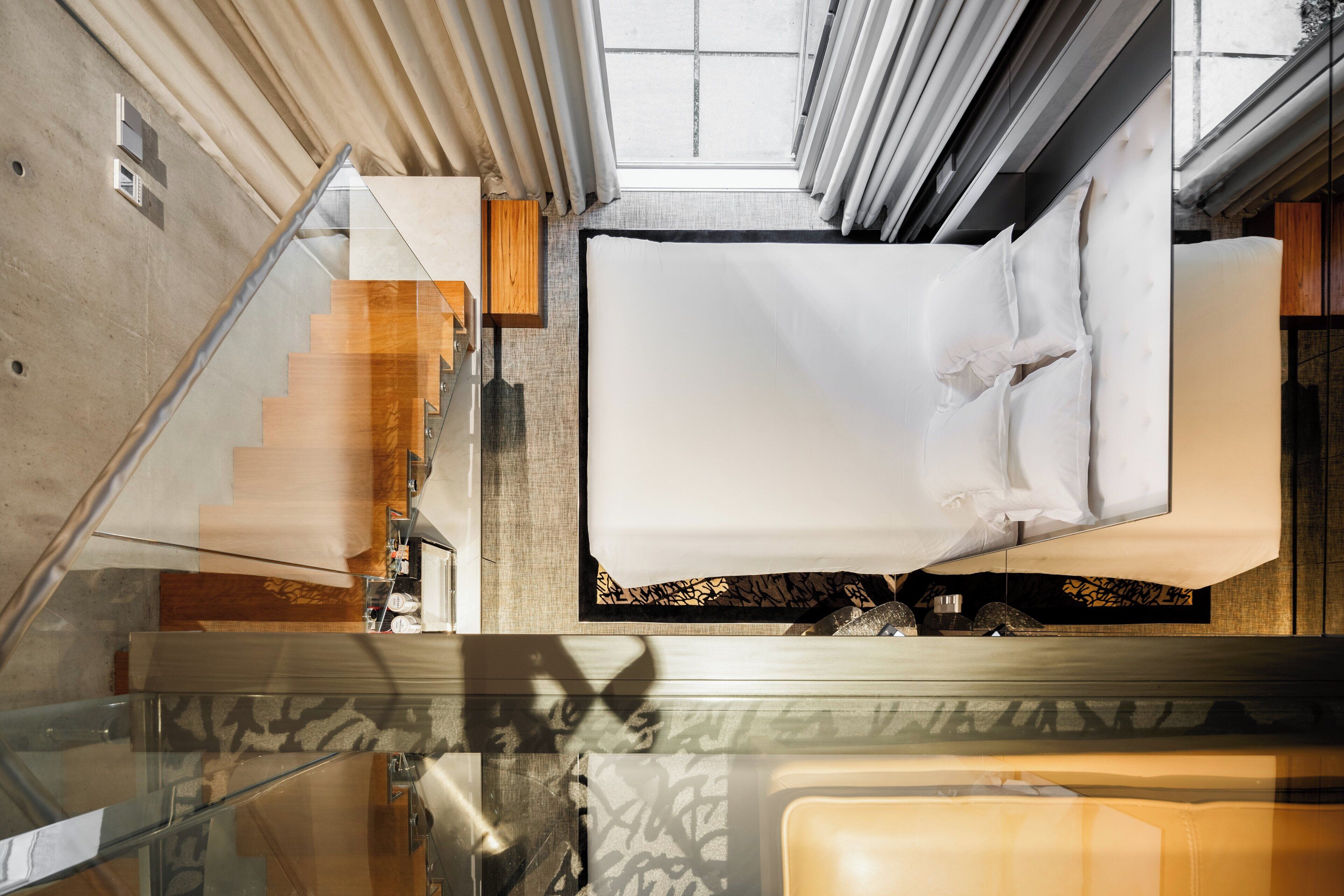 A modern hotel room with a large bed, a glass staircase, and a view of the sky through the ceiling.