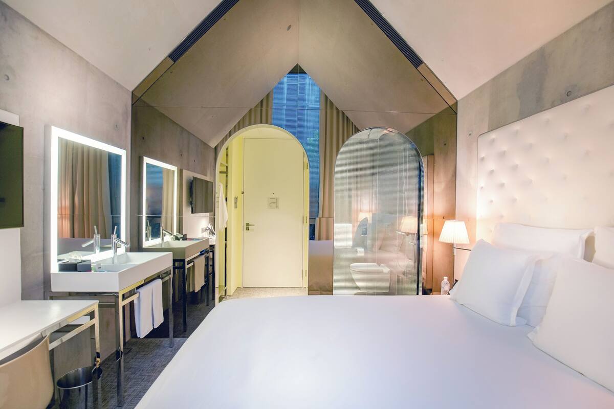 Een moderne hotelkamer met een groot bed, een badkamer met een spiegel, een wastafel en een deur naar een andere kamer.