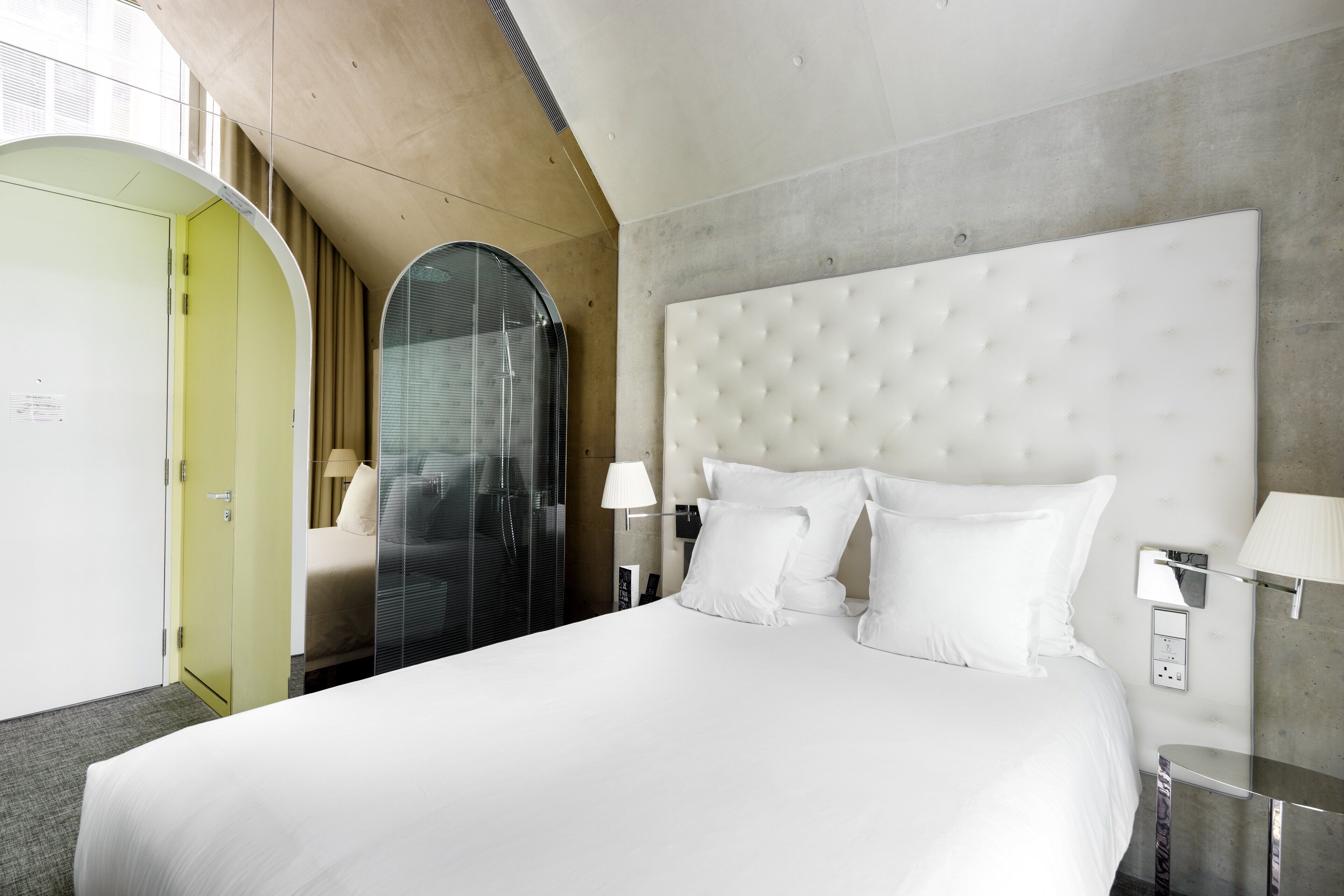 Ein modernes Hotelzimmer mit einem großen Bett, einer Glaskabinent Dusche und Blick auf die Stadt.
