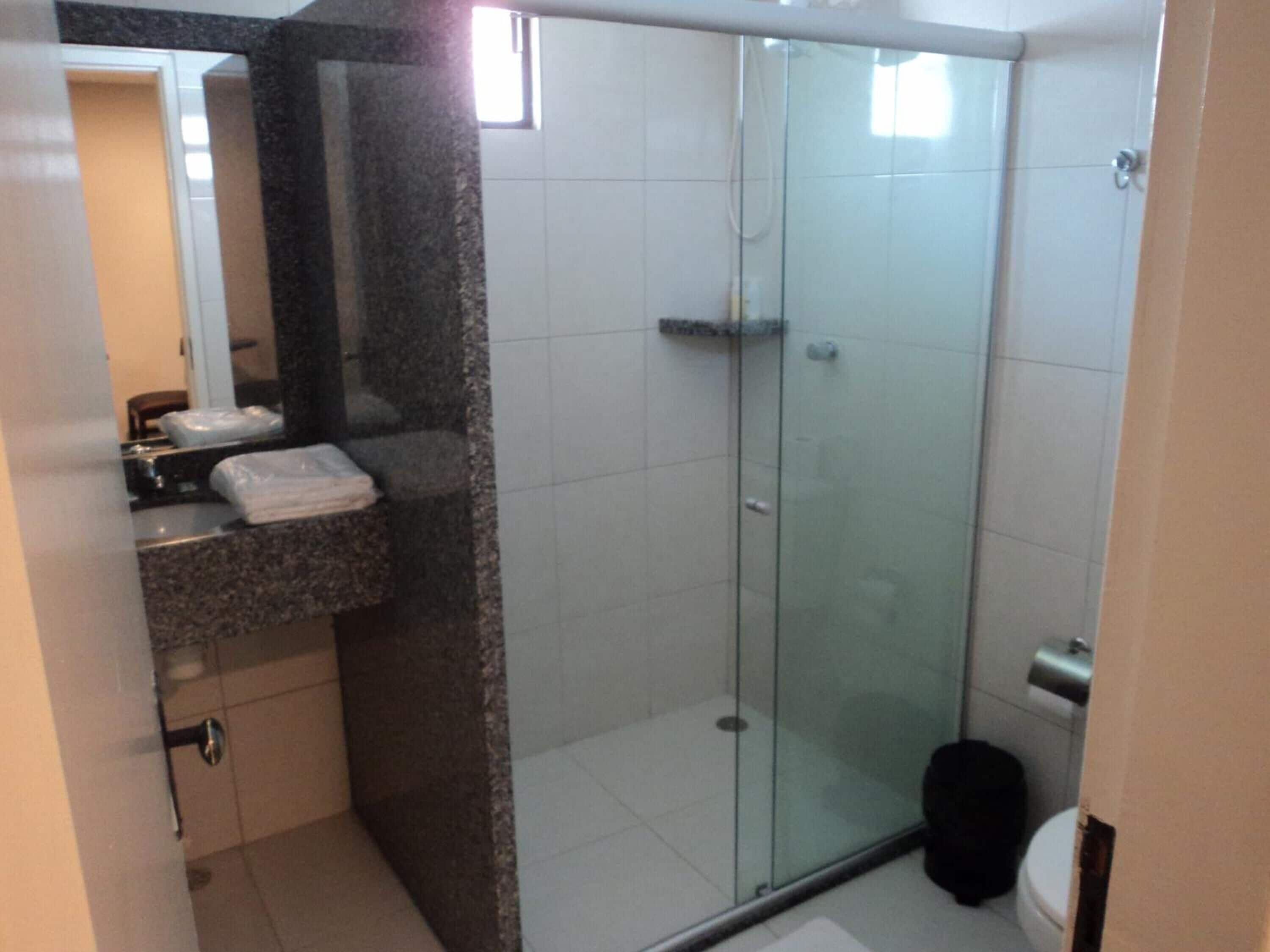 A bathroom with a glass shower enclosure, a sink with a marble countertop, and a toilet.