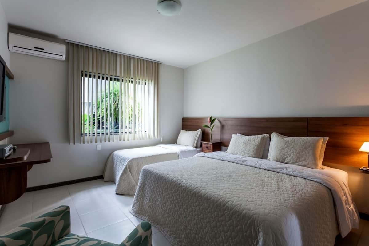 Une chambre d’hôtel avec deux lits, un bureau, une télévision et une fenêtre avec des stores.