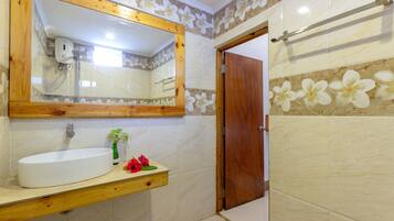 Baño con tocador de madera, un espejo grande y zona de ducha.