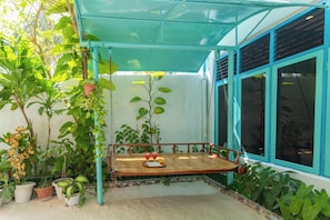 A covered outdoor seating area with a wooden bench, surrounded by potted plants and a window with blue trim. - Dream Inn Sun Beach Hotel (Thulusdhoo Island)
