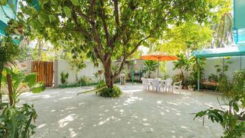 Un patio al aire libre con una mesa y sillas, rodeado de plantas en macetas y un árbol grande.