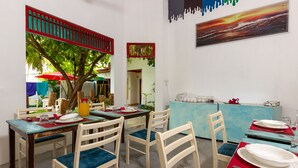 Un comedor con una mesa dispuesta para cuatro, sillas con cojines azules, un paraguas rojo y vistas al exterior.