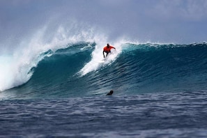 A surfer in a red shirt riding a large wave in the ocean. - Dream Inn Sun Beach Hotel (Thulusdhoo Island)
