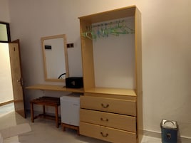 Een kamer met een houten bureau, een spiegel, een kleine koelkast en een blauwe prullenbak.
