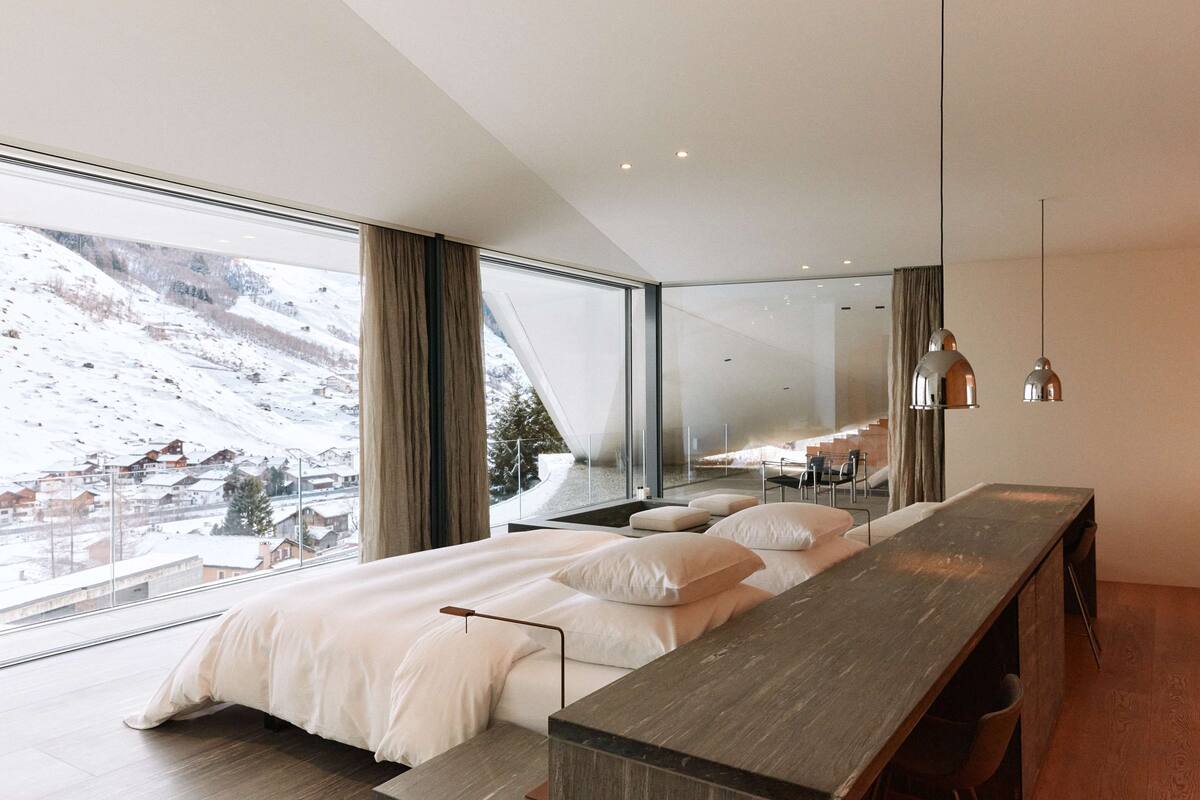 Une chambre moderne avec un grand lit, un banc en bois et une vue sur un paysage enneigé.