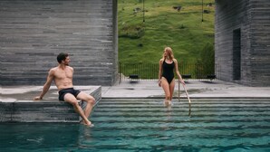 A man and a woman by a pool with a view of a green hillside. - 7132 Hotel (Vals)