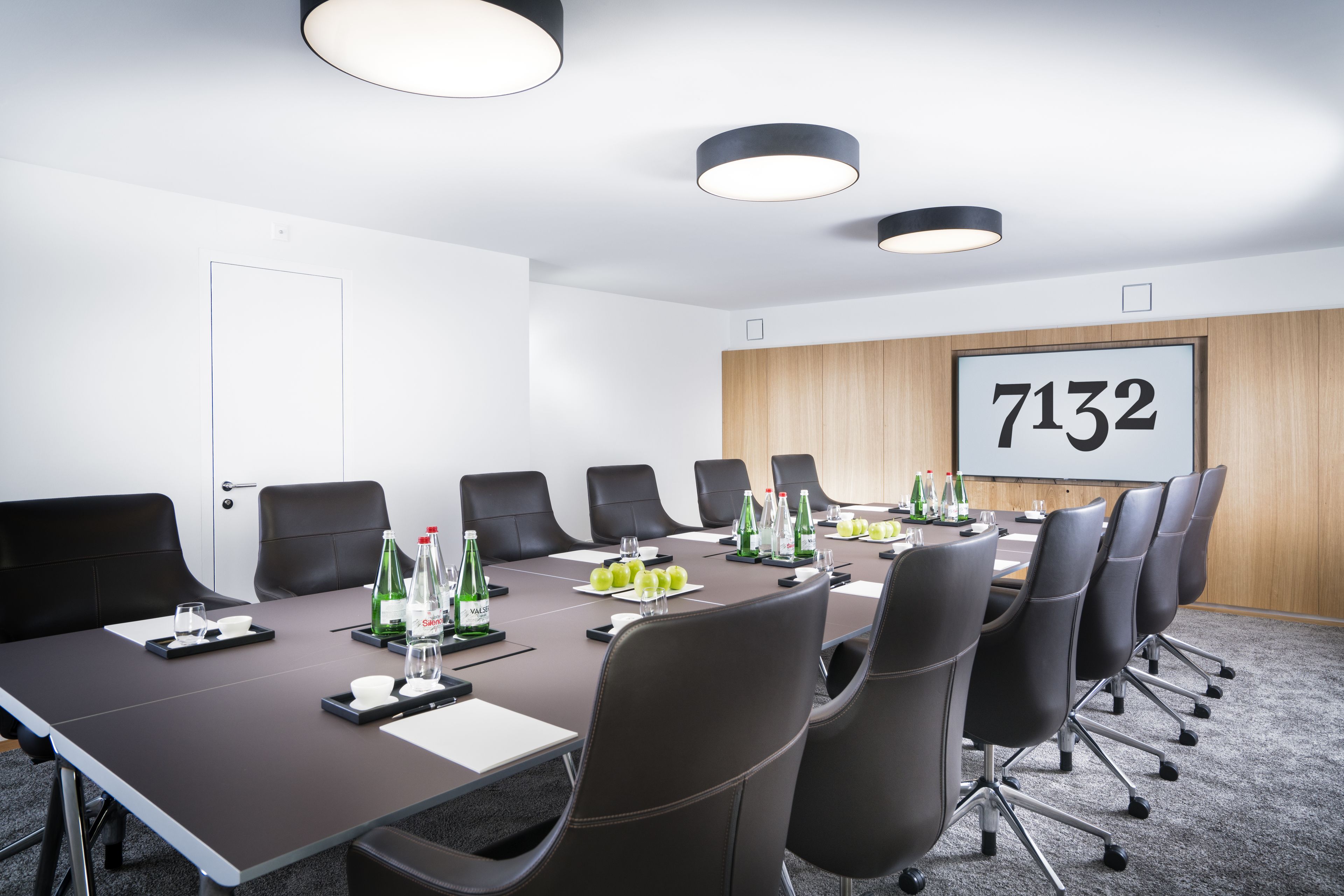 A conference room with a long table, multiple chairs, and a projector screen displaying the number 7132.