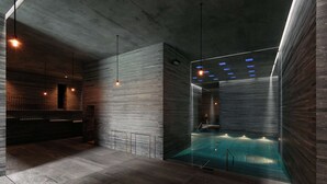 A modern indoor swimming pool with a minimalist design, featuring a concrete ceiling and walls, and a glass enclosure for the pool area. - 7132 Hotel (Vals)