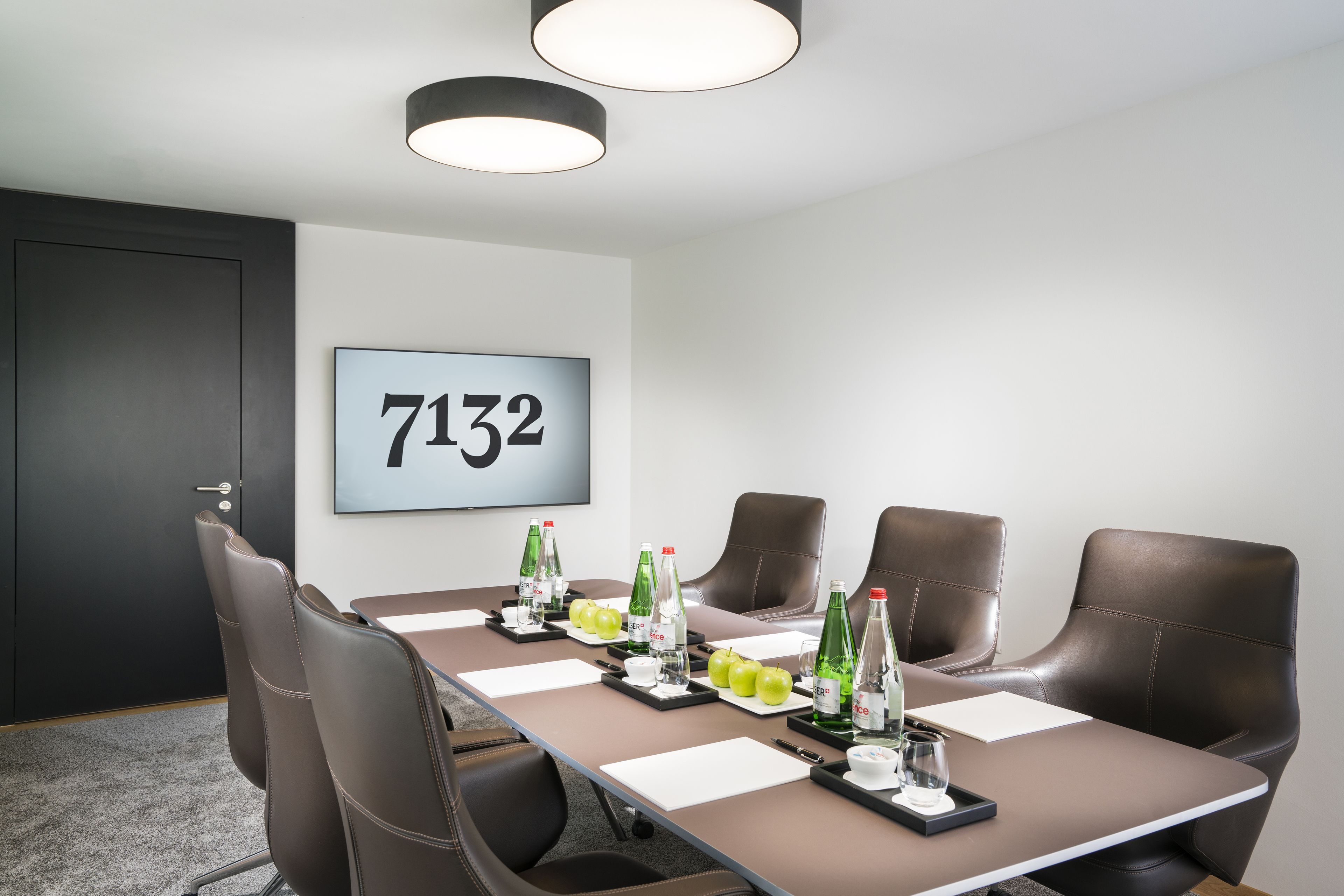 Ein Konferenzraum mit einem langen Tisch, vier Stühlen und einem Nummernschild an der Wand.