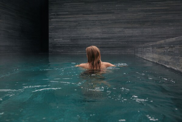 A person in a swimming pool with a stone wall background. - 7132 Hotel (Vals)